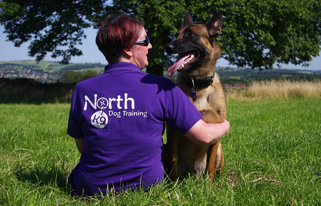 A woman with her back to the camera shares a look with her dog, a Belgian Malinois facing the camera